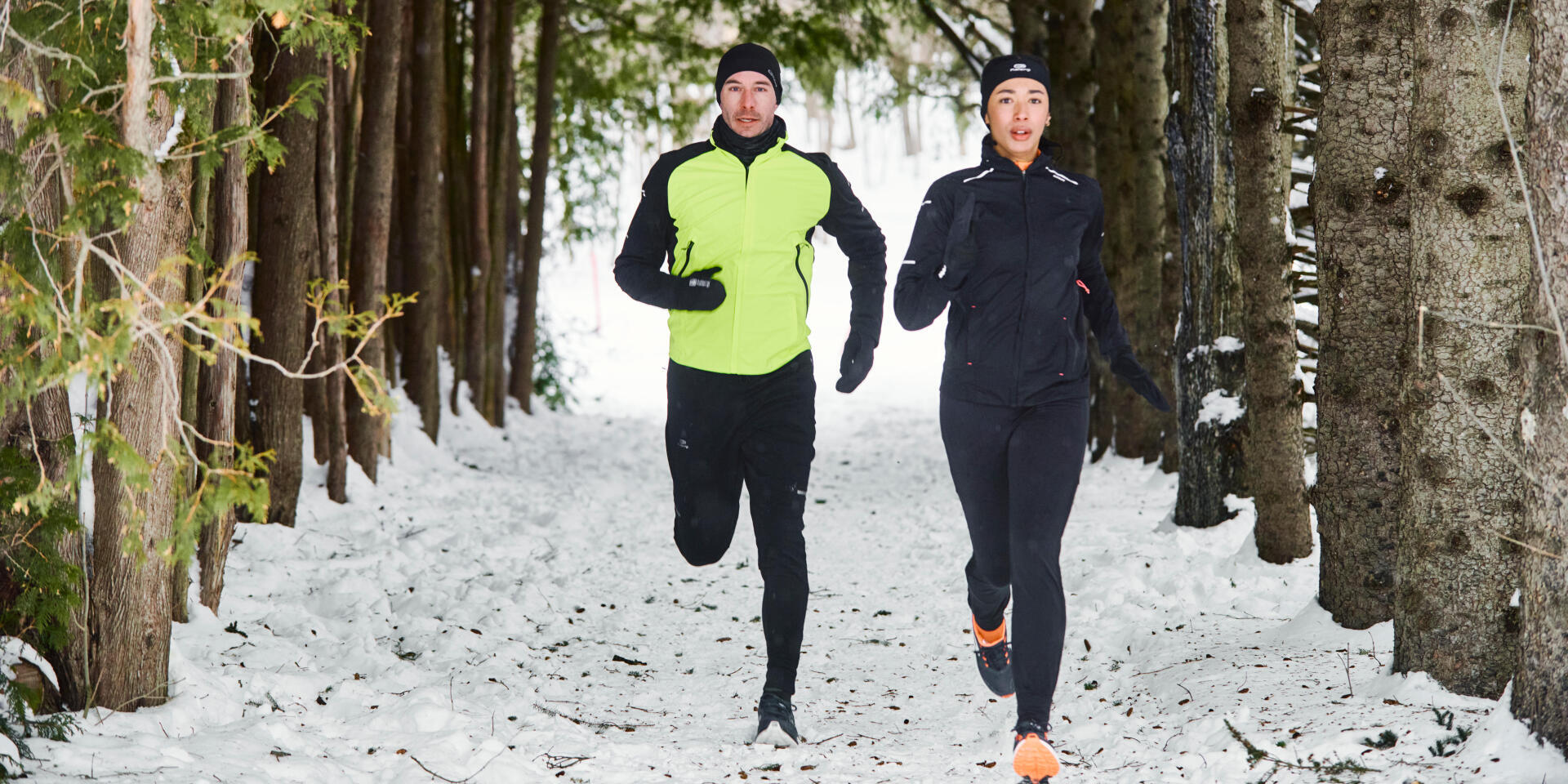Man and woman running side by side in the woods , in snow. 