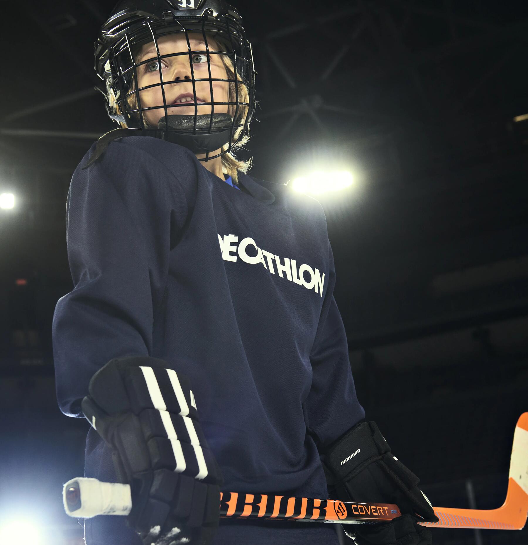 chłopiec stojący na lodowisku w kasku i i stroju hokejowym trzymając kij hokejowy w rękach