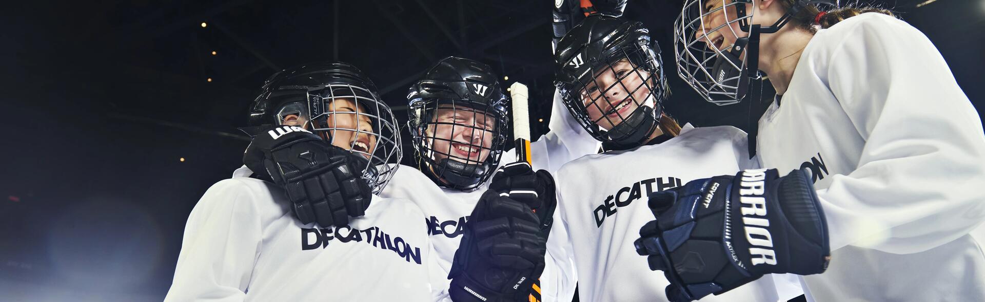 dzieci stojące w kaskach i rękawicach hokejowych  z kijami hokejowymi w rękach