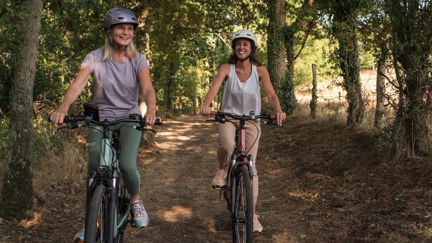 duas mulheres a andar de bicicleta na natureza, com capacete