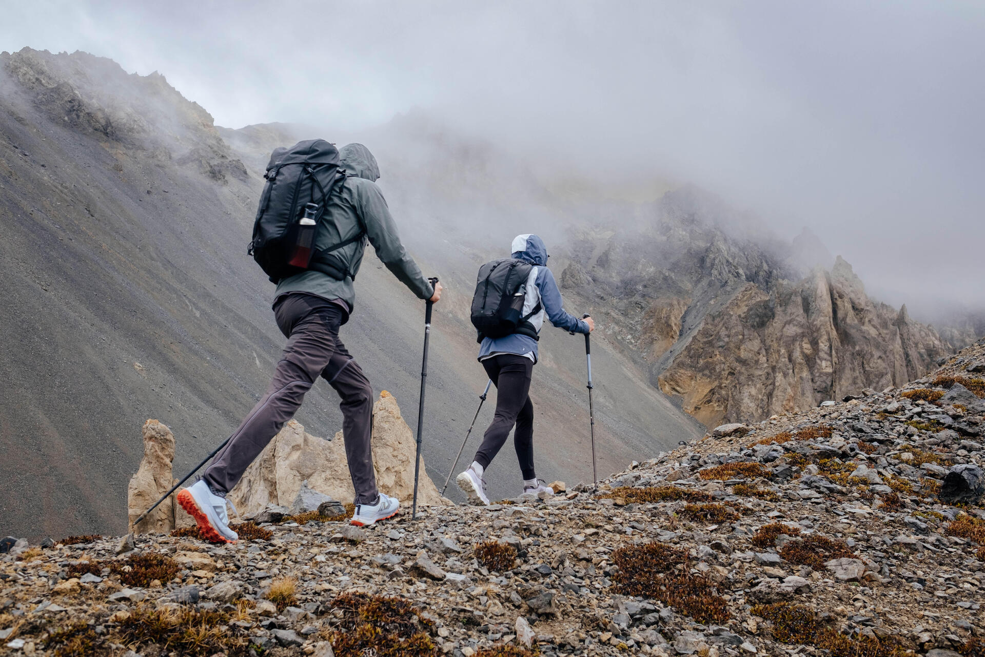Dwie osoby w odzieży sportowej w butach trekkingowych chodzące po górach