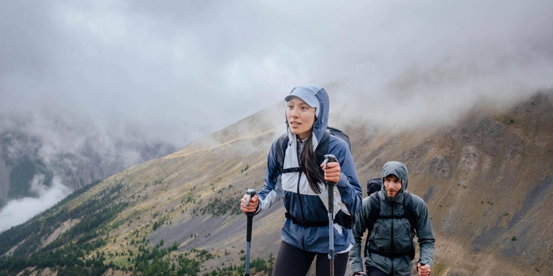 kobieta i mężczyzna wędrujący po górach w kurtkach trekkingowych z kijami trekkingowymi w rękach