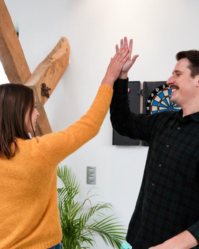Eine Frau und ein Mann geben sich vor einer Dartscheibe ein High-Five.