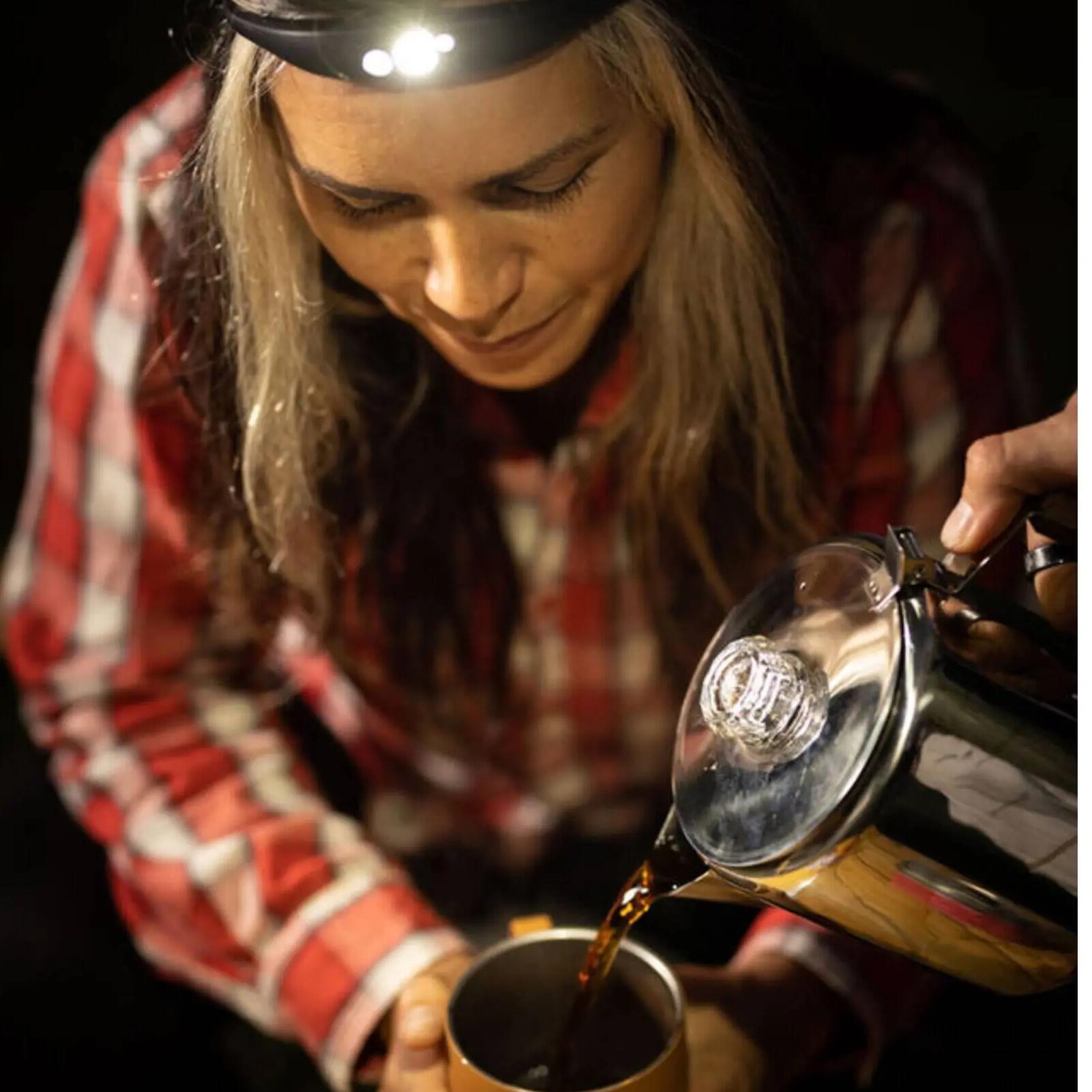 kobieta z latarką czołówką na głowie trzymająca kubek turystyczny z napojem