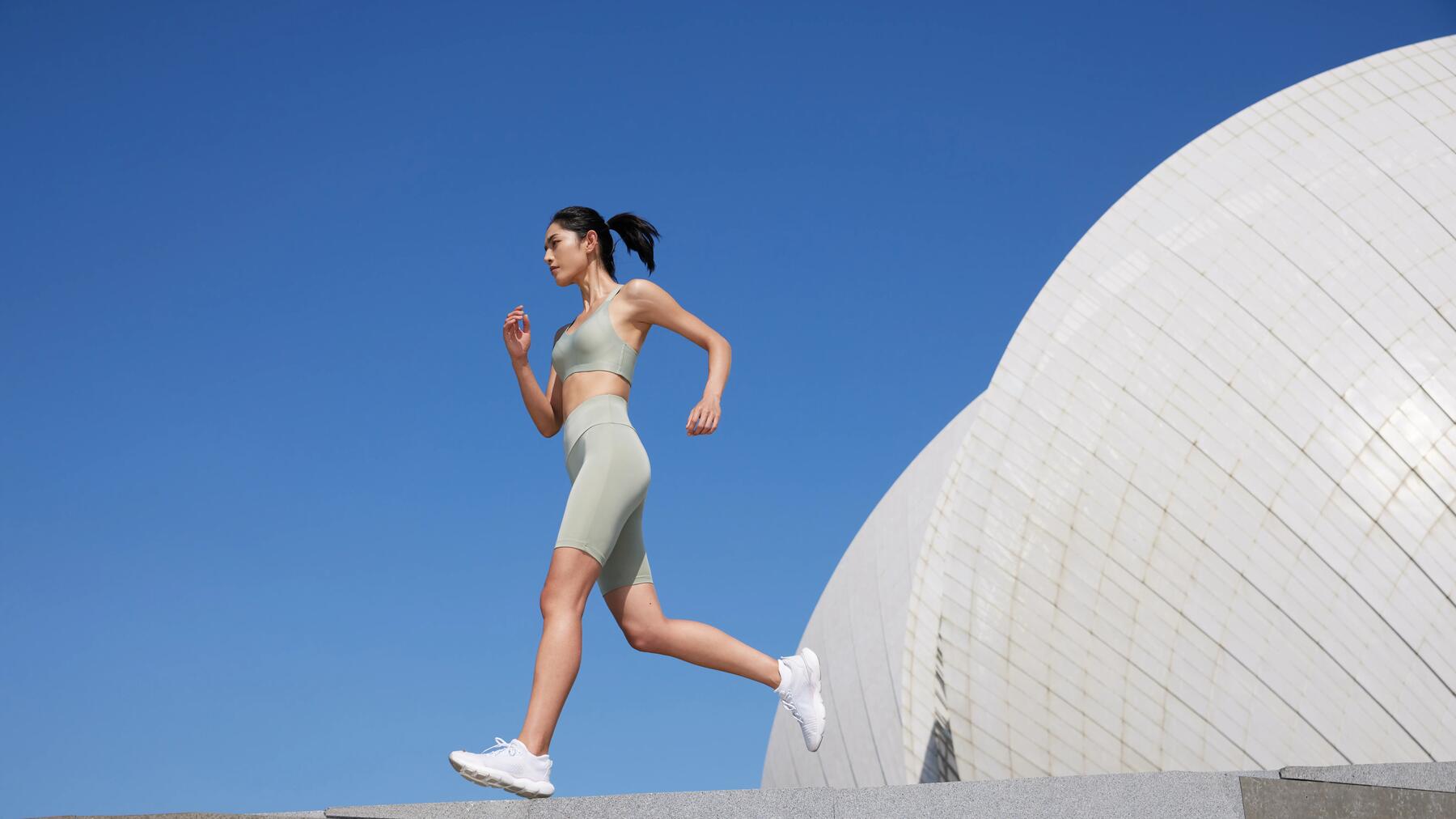 Frau in heller Sportkleidung joggt vor moderner, runder Architektur bei klarem, blauem Himmel.