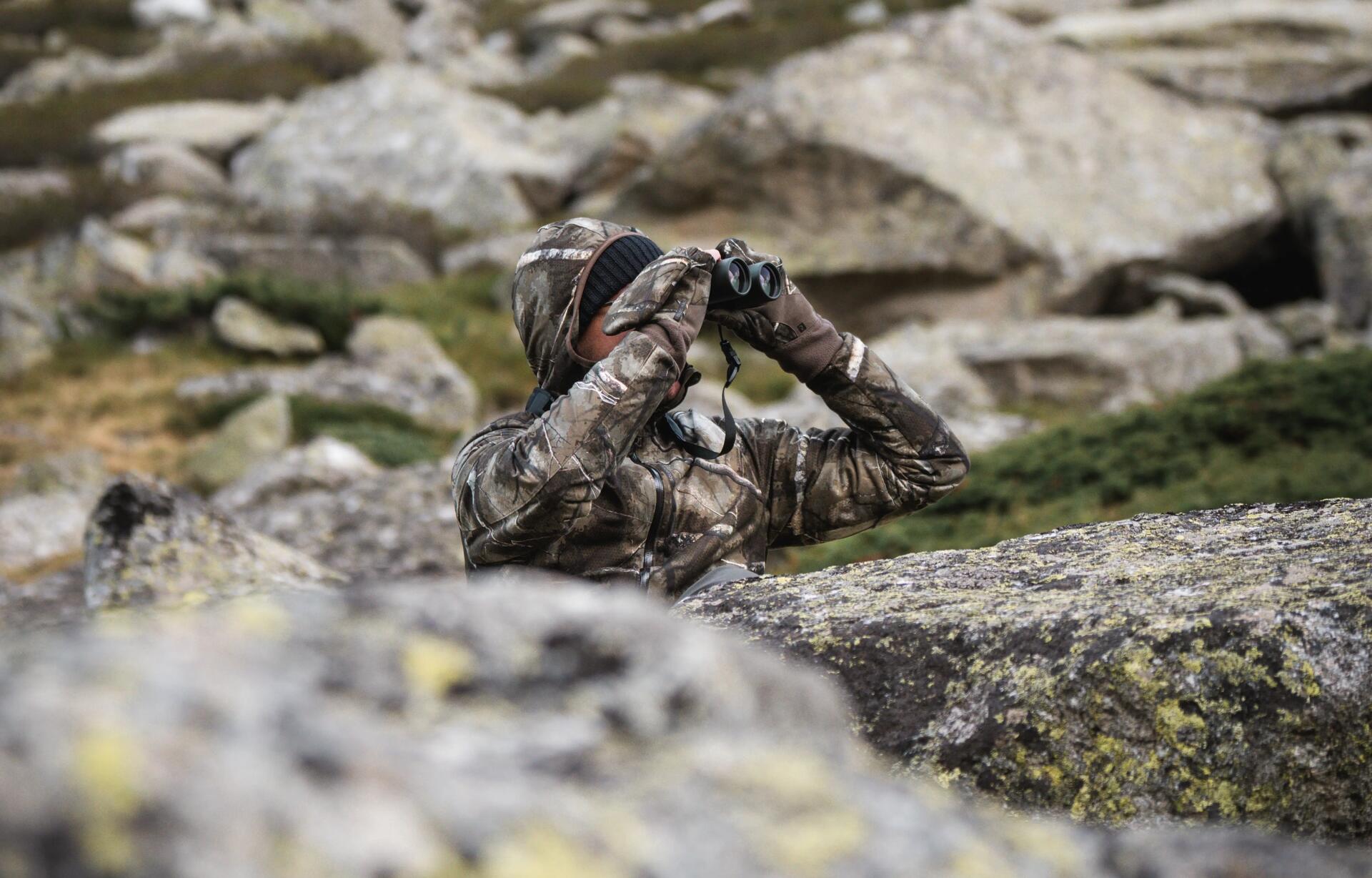 Observer aux jumelles en plein montagne camouflé au milieu des rochers