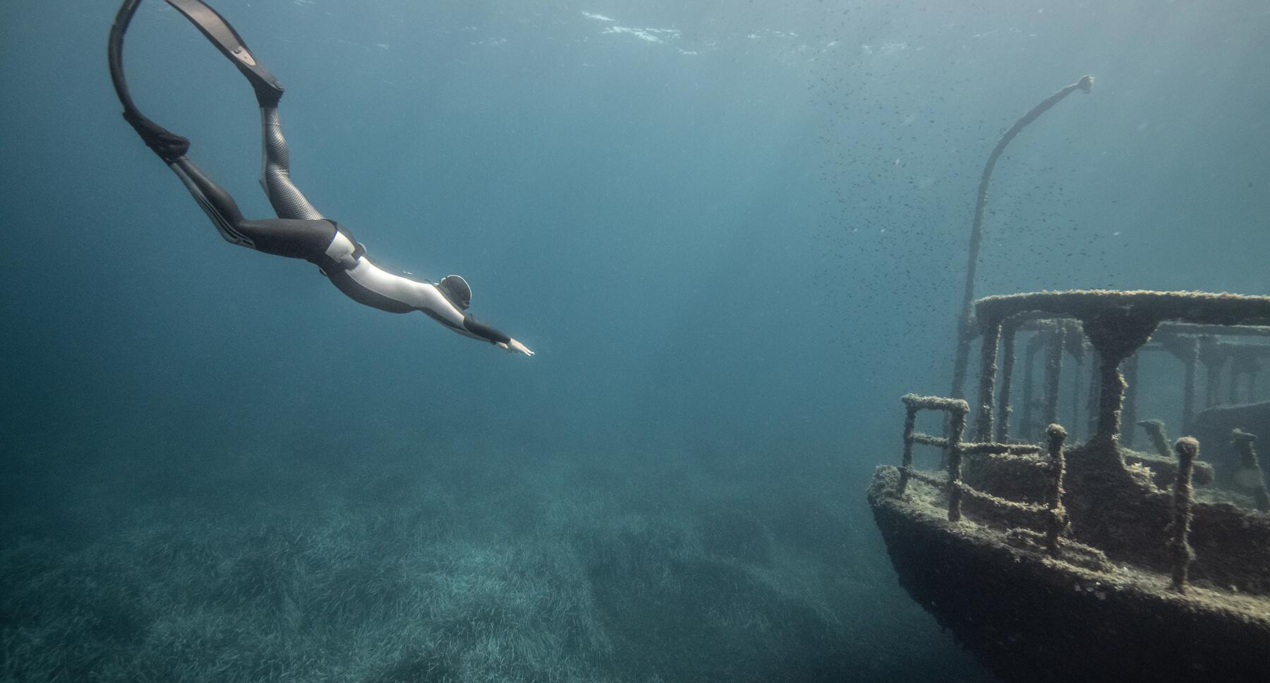 mężczyzna nurkujący w stronę wraku w kombinezonie i płetwach do freedivingu