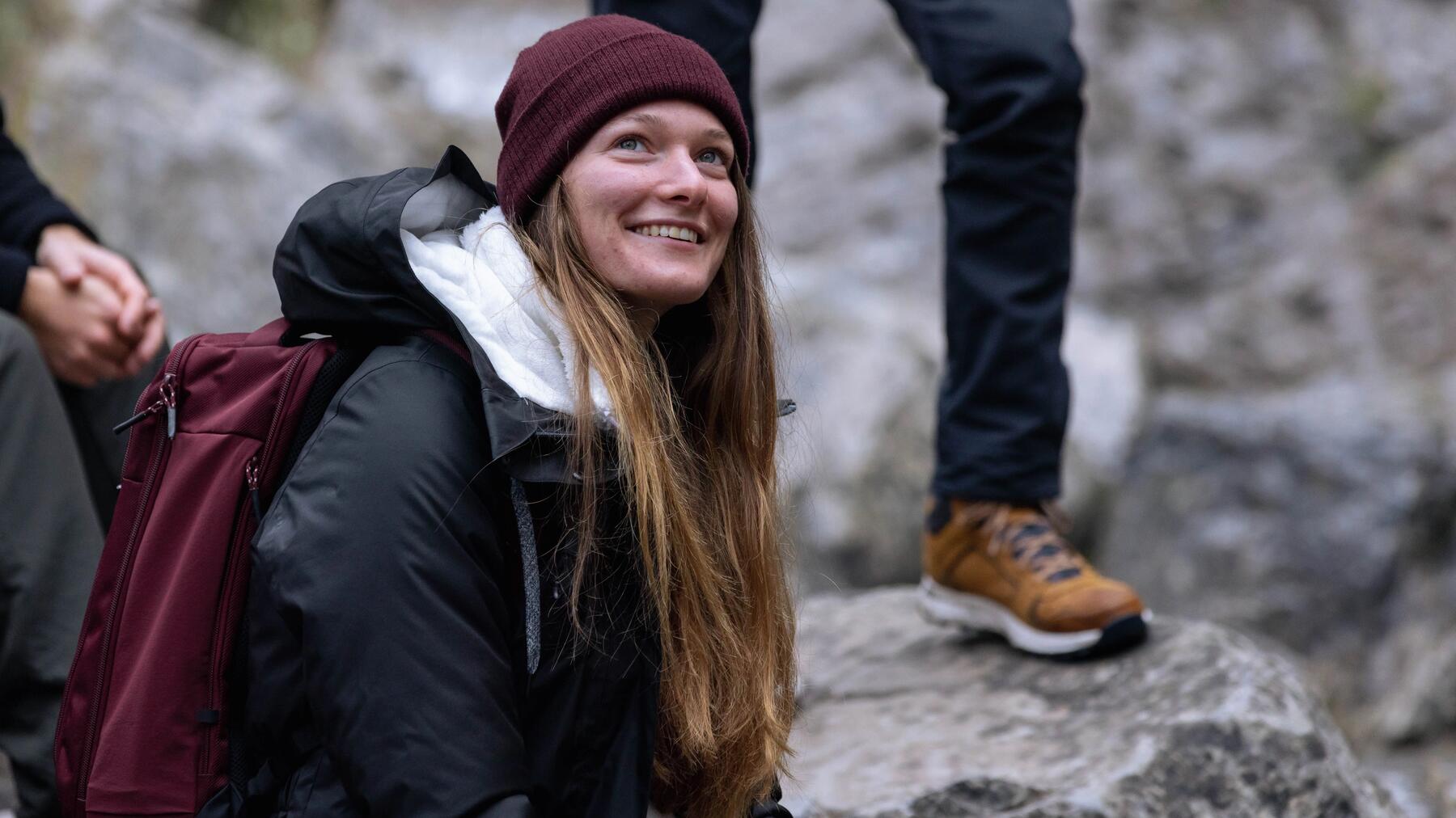 Kobieta w bordowej czapce i czarnej kurtce siedząca na skale