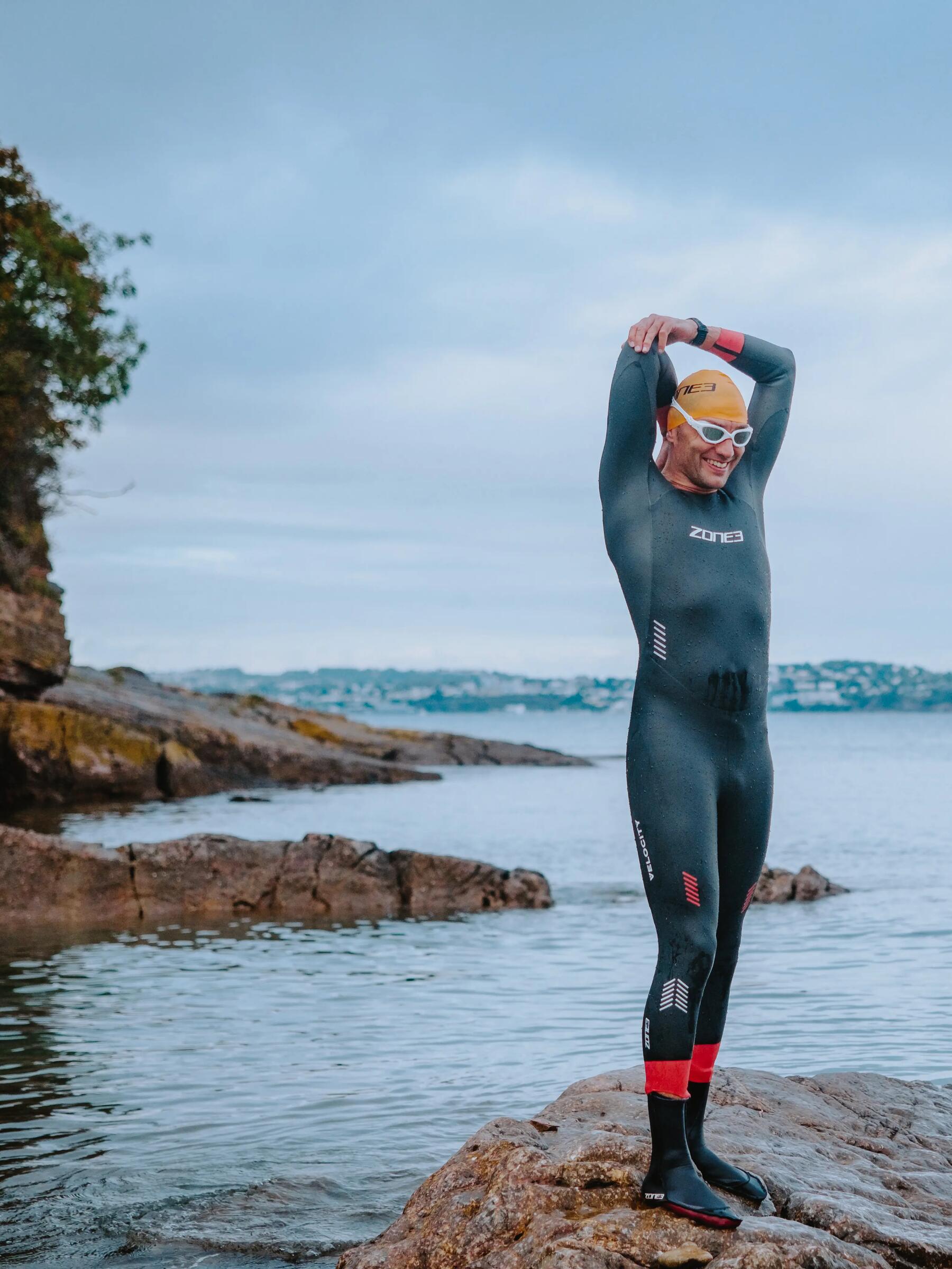 man wearing a wetsuit stretching by the sea