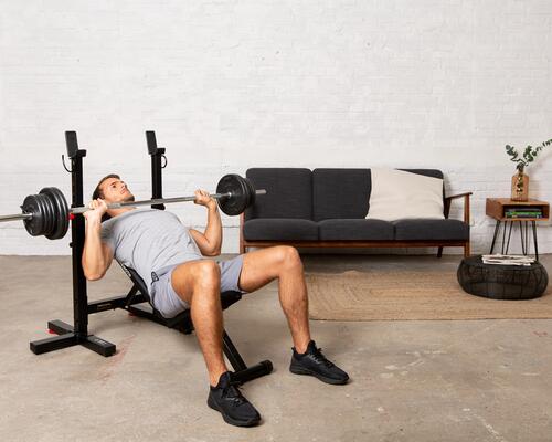 Mężczyzna w odzieży fitness wykonujący ćwiczenia na klatkę piersiową ze sztangą