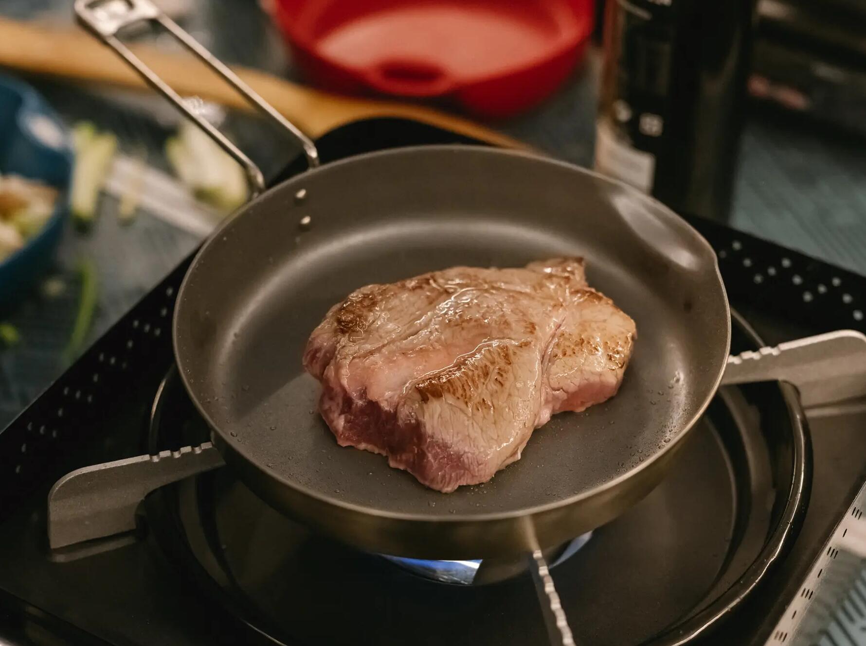 porcja mięsa smażąca się na patelni stojącej na kuchence turystycznej