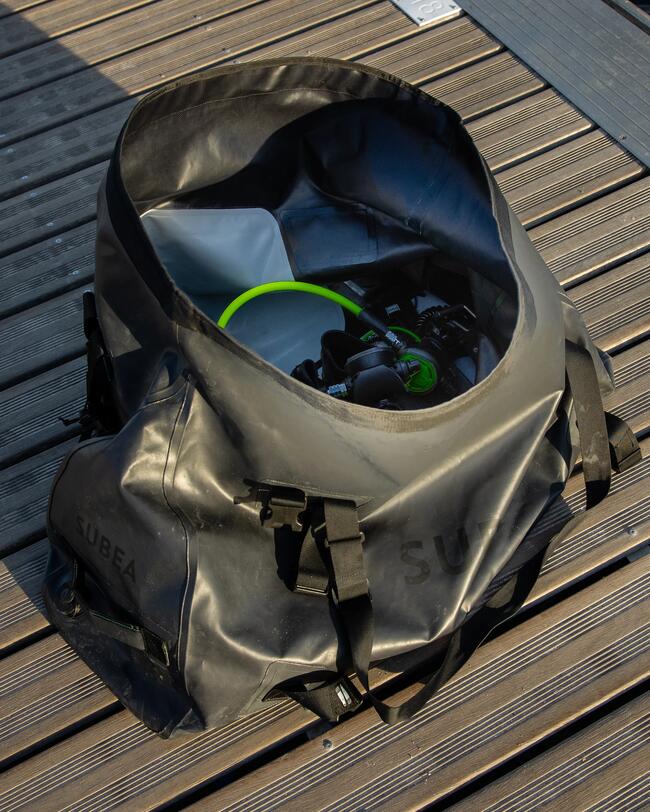 Schwarze Tasche auf Holzboden, enthält Tauchausrüstung, Texturen von glattem Stoff und Holzmaserungen.