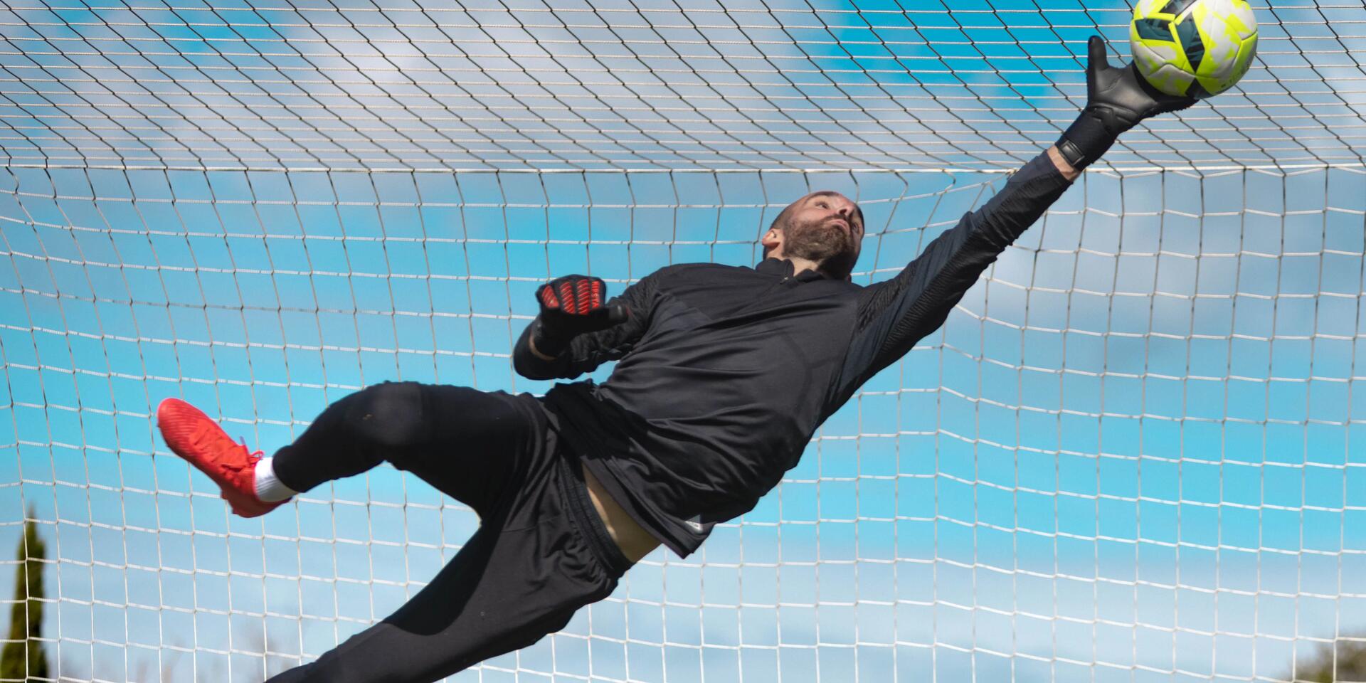 bramkarz w odzieży i rękawicach bramkarskich łapiący piłkę