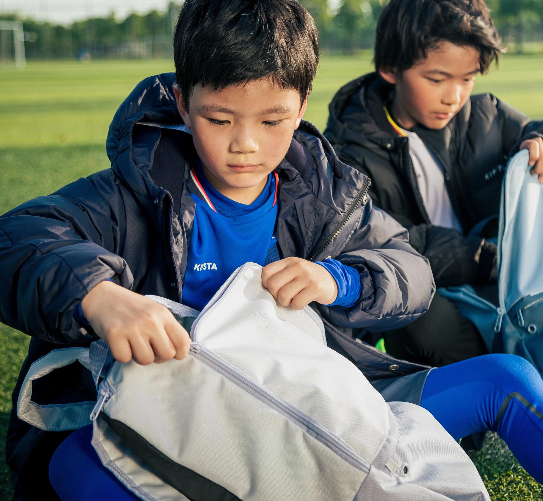dzieci siedzące na trawie i otwierające plecaki szkolne