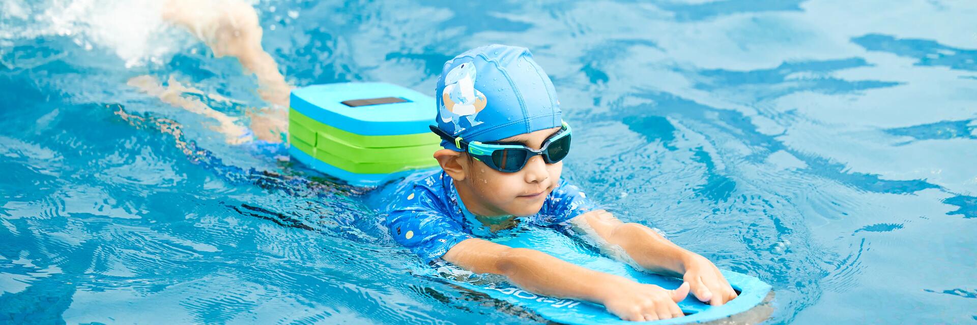 Dziecko uczące się pływać z deską ubrane w czepek i okulary do pływania