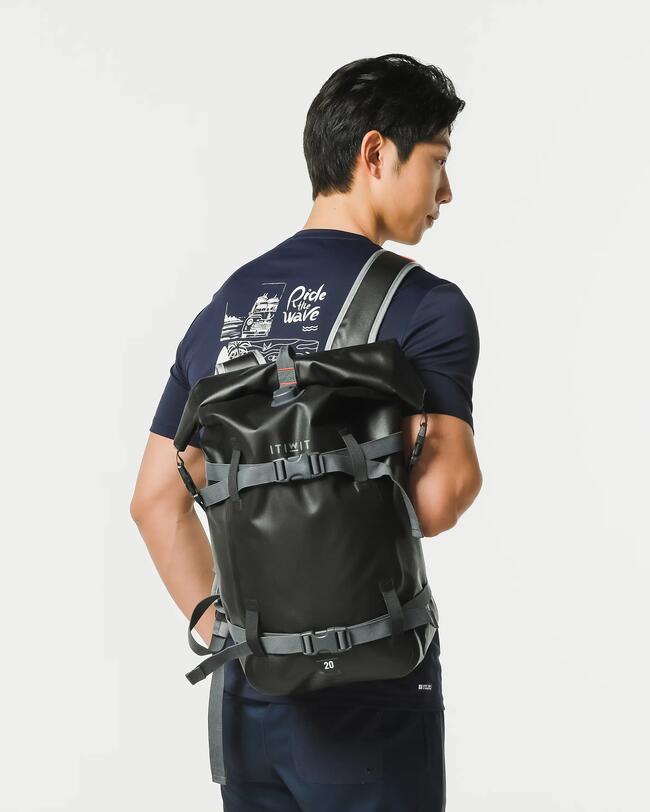 Mann in blauem T-Shirt mit schwarzem Rucksack, graue Riemen, helle Hintergrund.