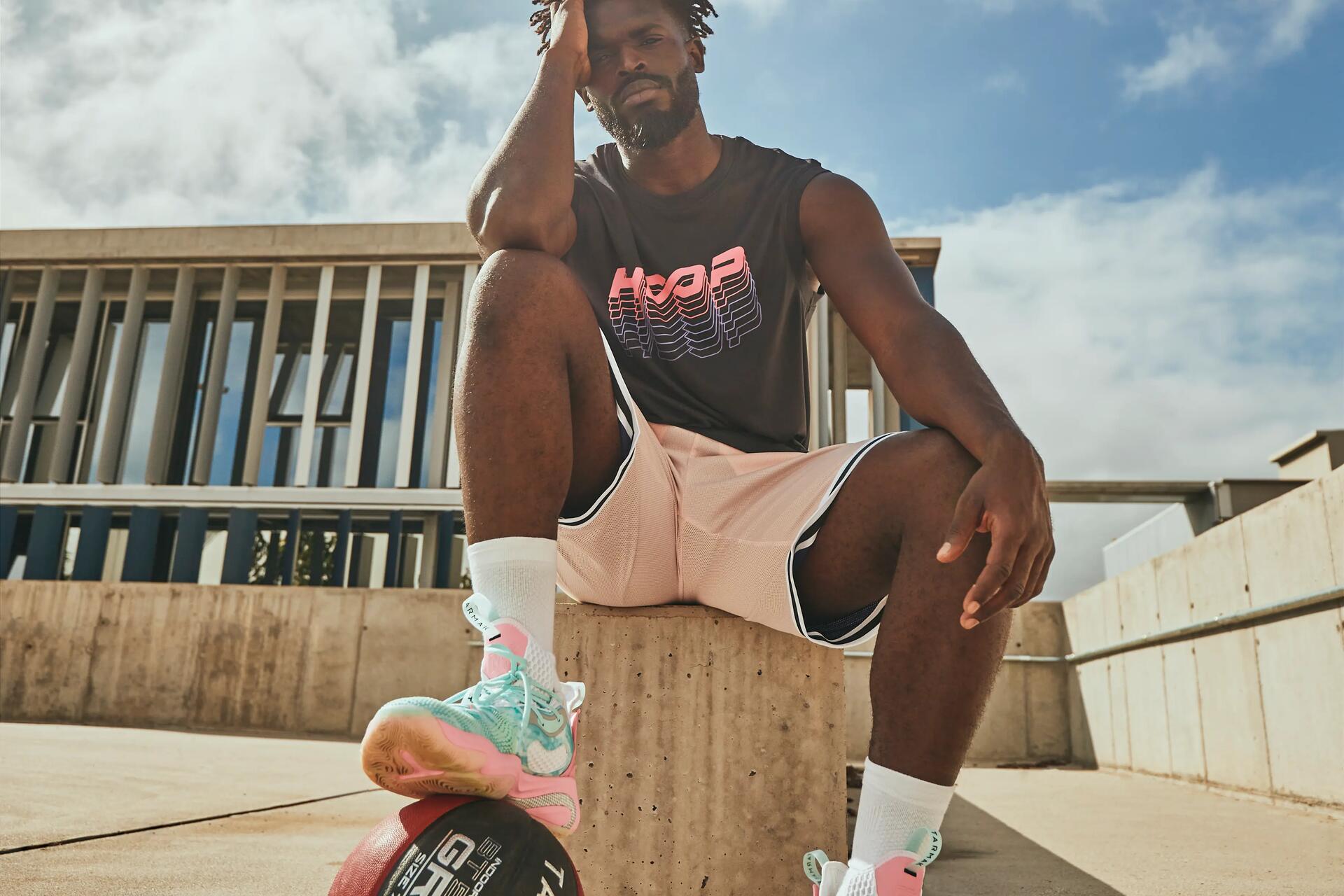 mężczyzna siedząćy w odzieży do gry w koszykówkę trzymając nogę na piłce  do koszykówki
