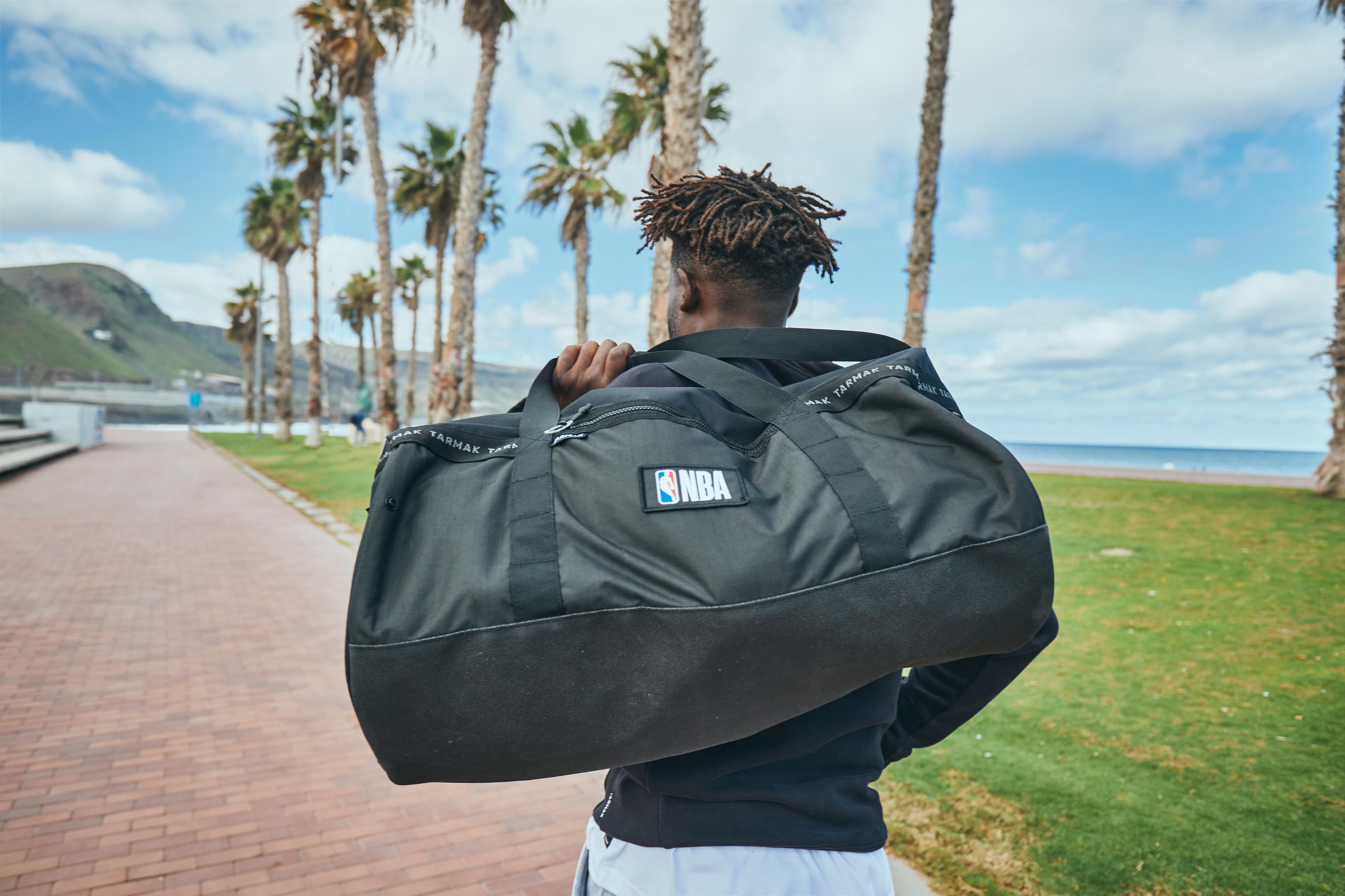 Athlete carrying a large black sports duffle bag over his shoulder outdoors.