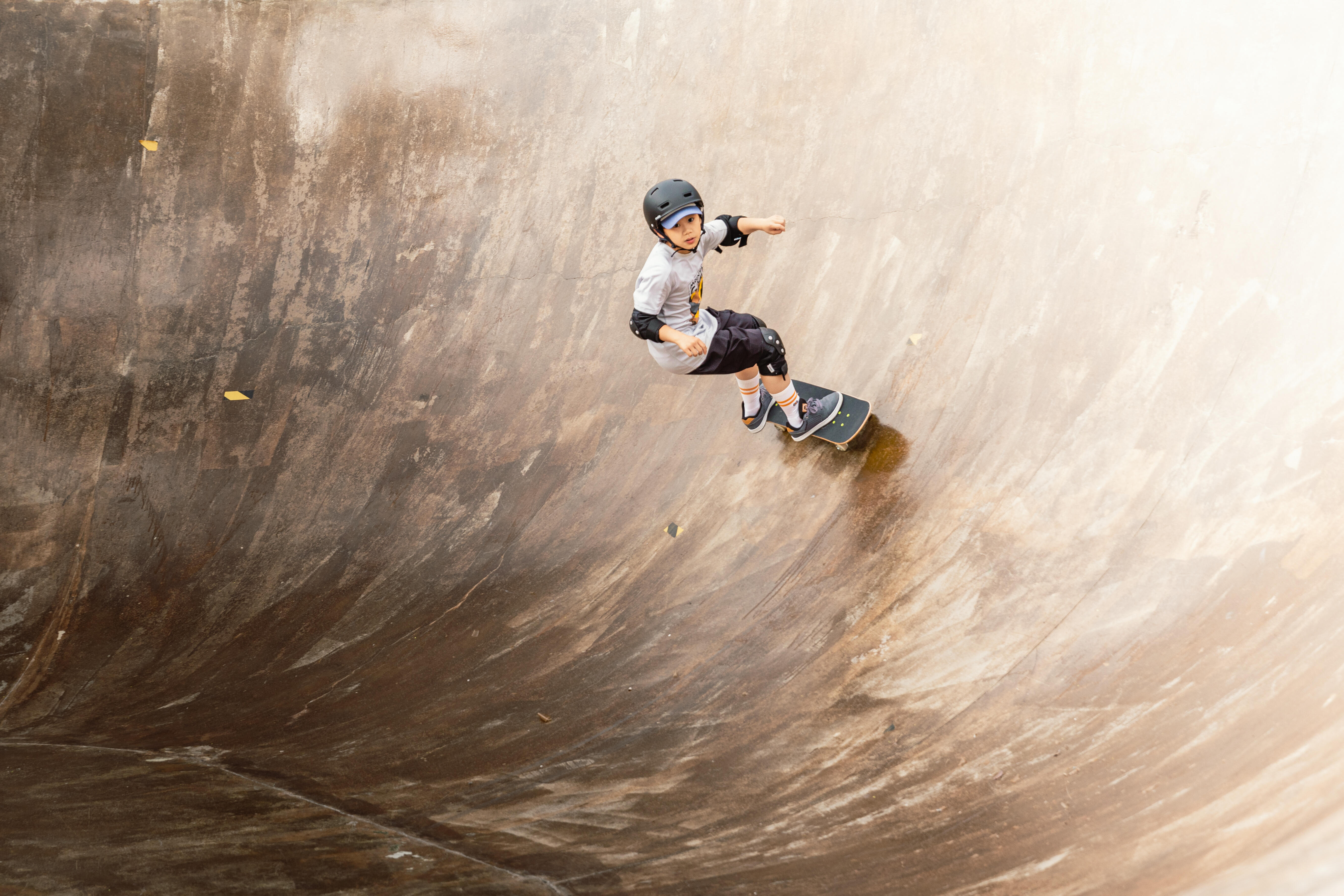 Boy in helmet riding skateboard down a curved concrete ramp