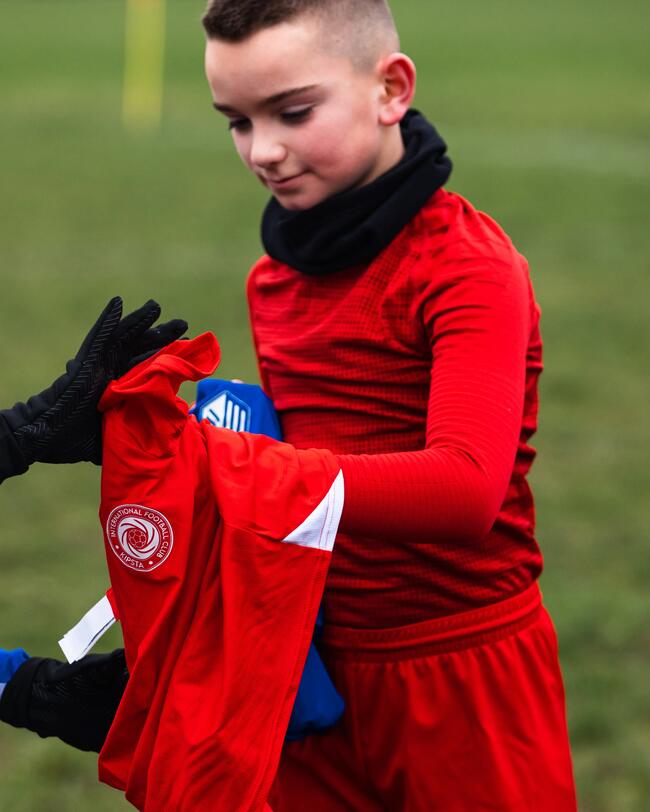 Junge im roten Keepdry Shirt und Schlauchschal auf Fußballfeld.