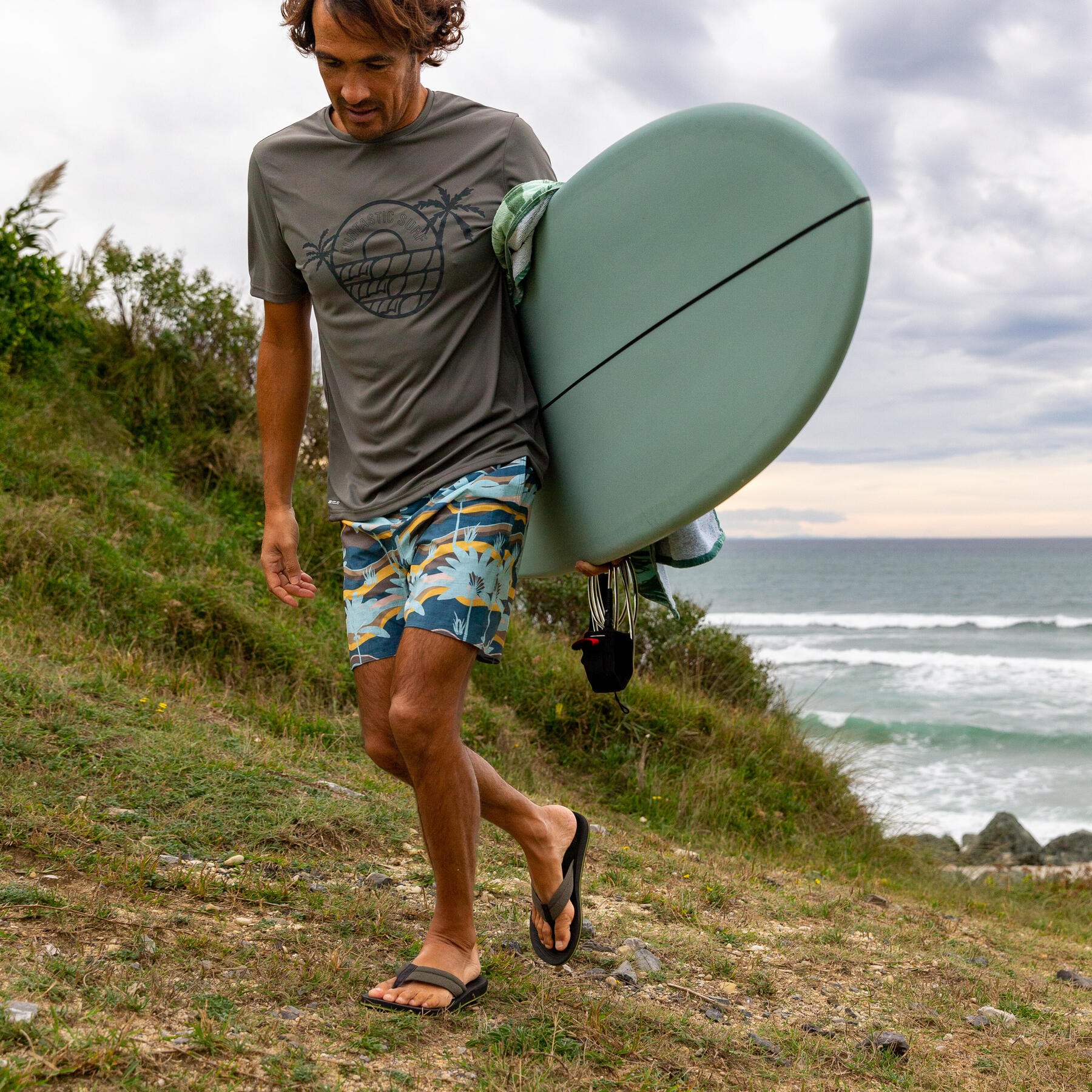 Mężczyzna idący na plażę w japonkach z deską surfingową
