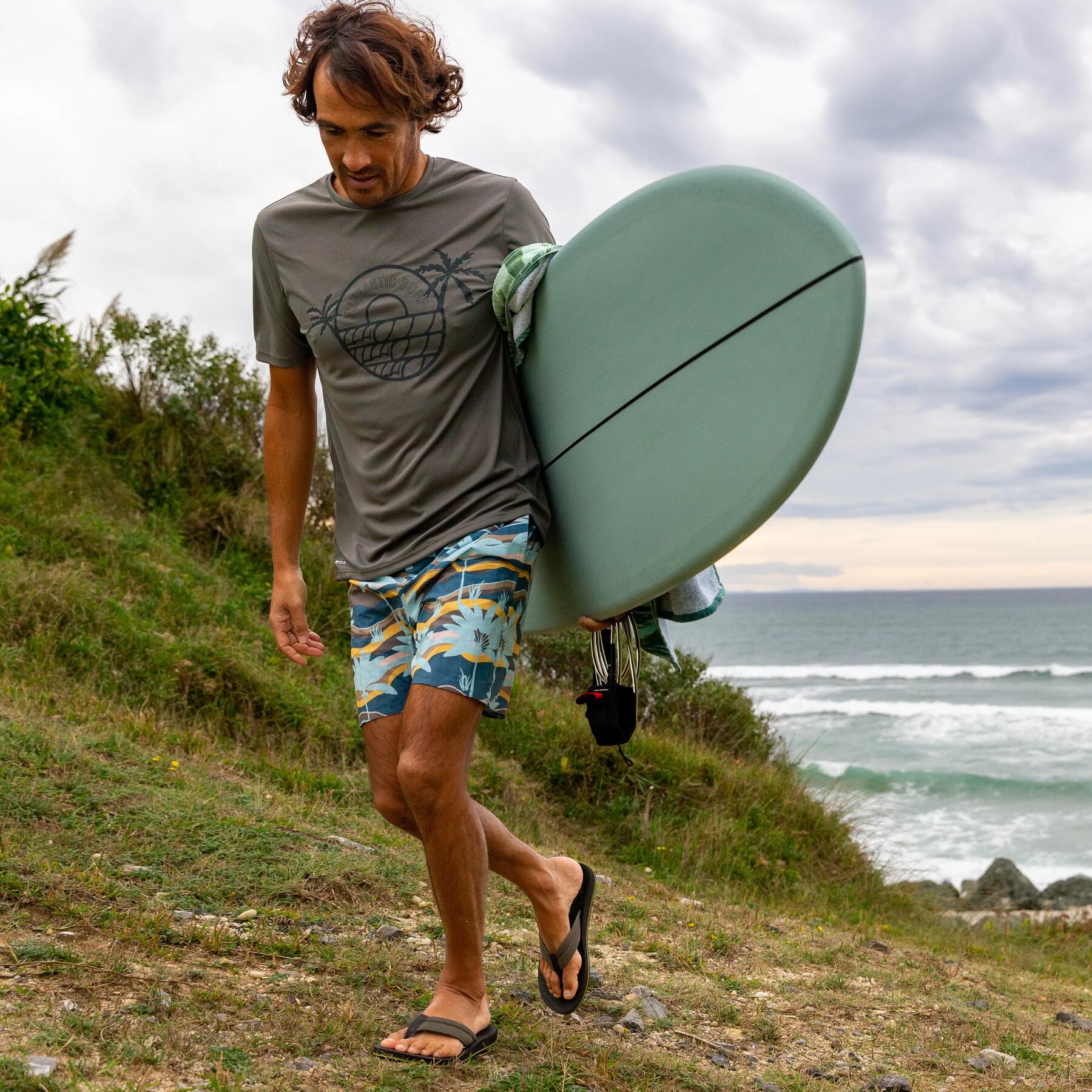 Mężczyzna ubrany w japonki idący na plażę z surfingiem