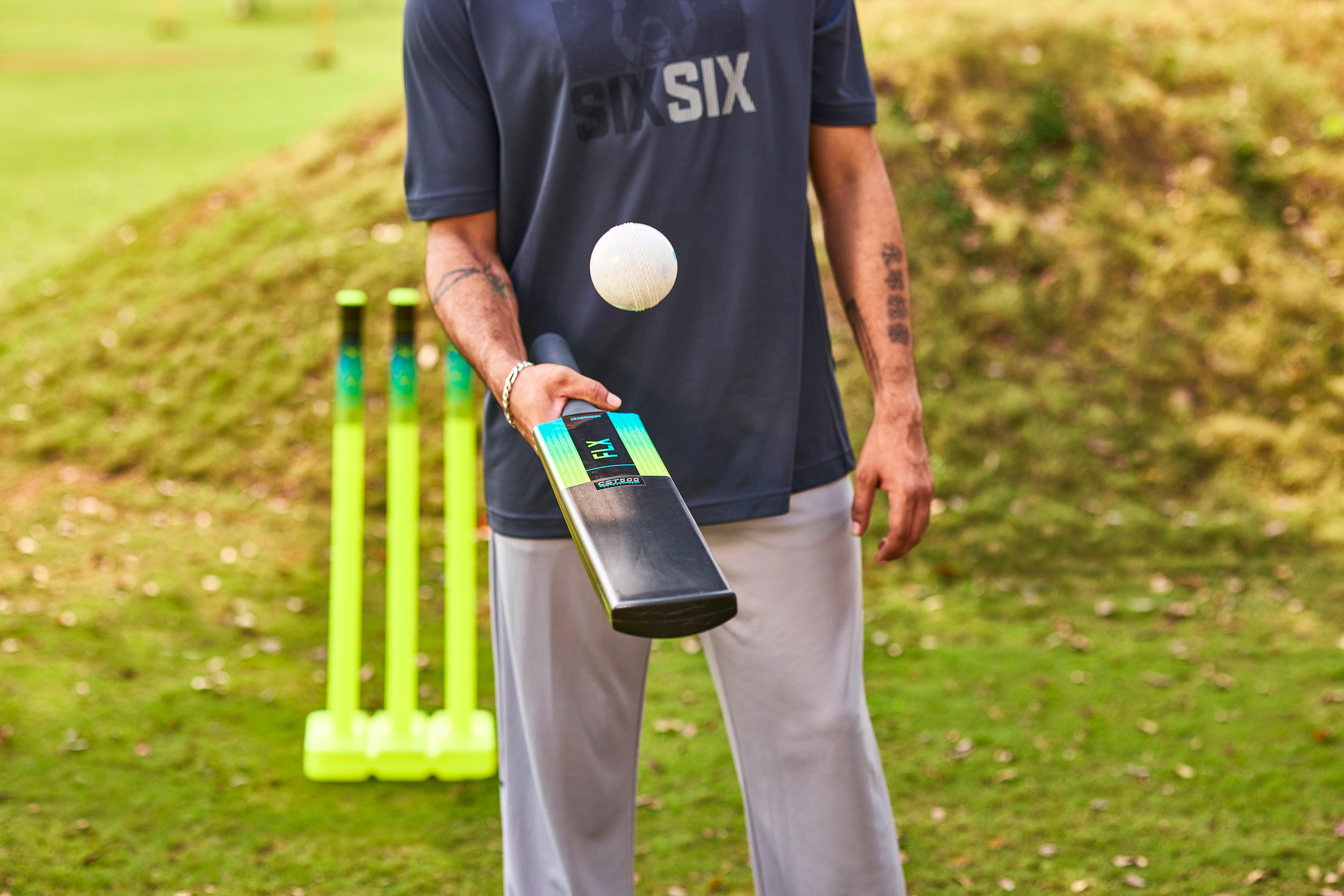 Cricket bat with teal design held by man near yellow wickets