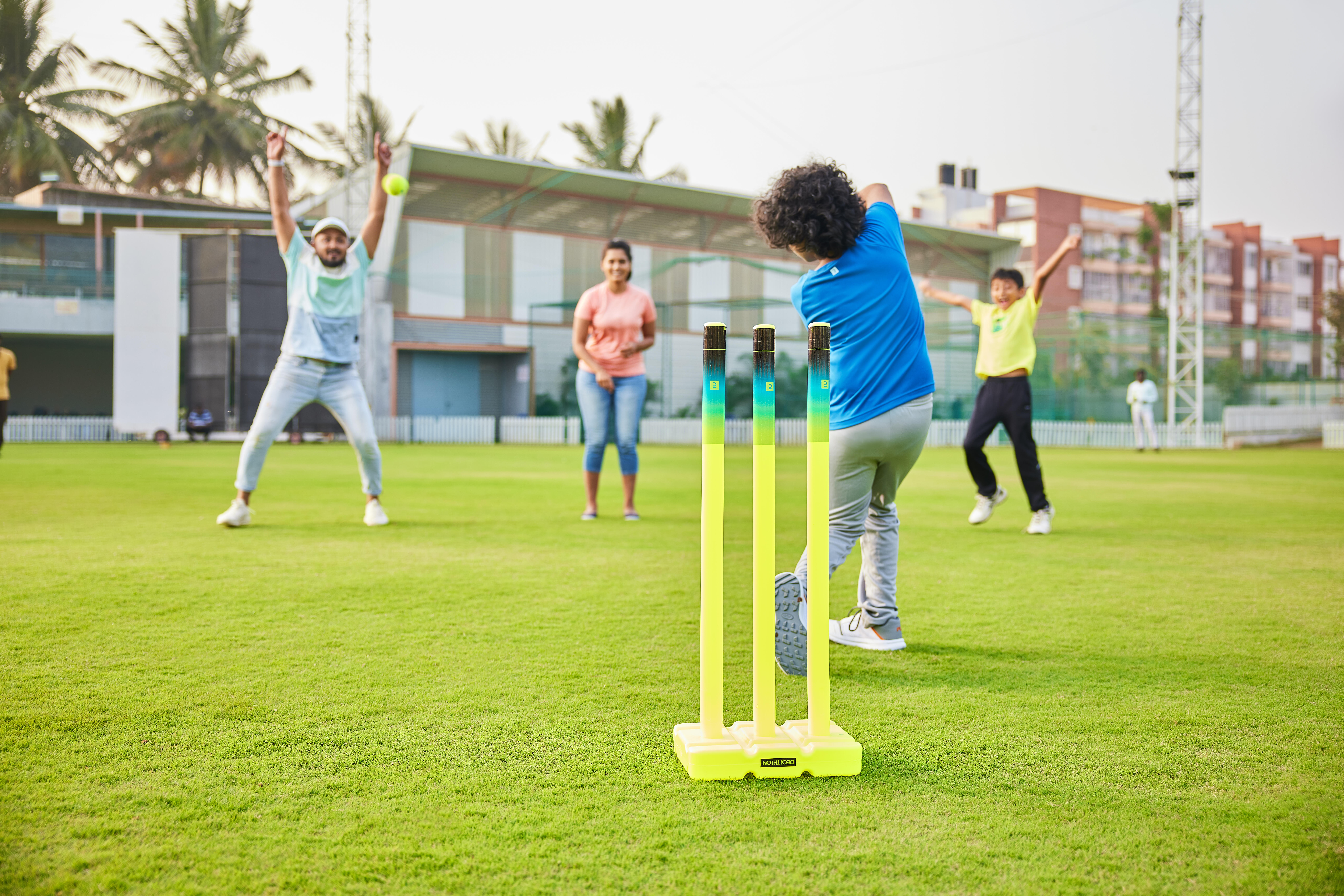 Group playing cricket on a field with yellow wickets in centre