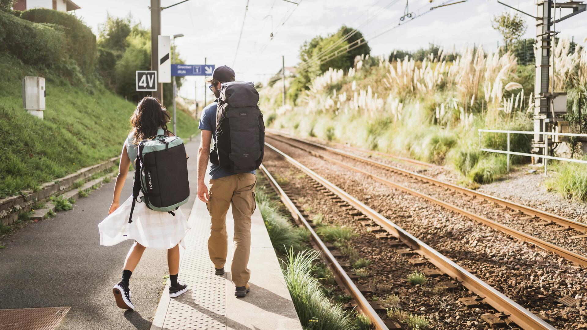 Kobieta i mężczyzna z plecakami turystycznymi wybierający się na city break wędrując przy torach kolejowych 