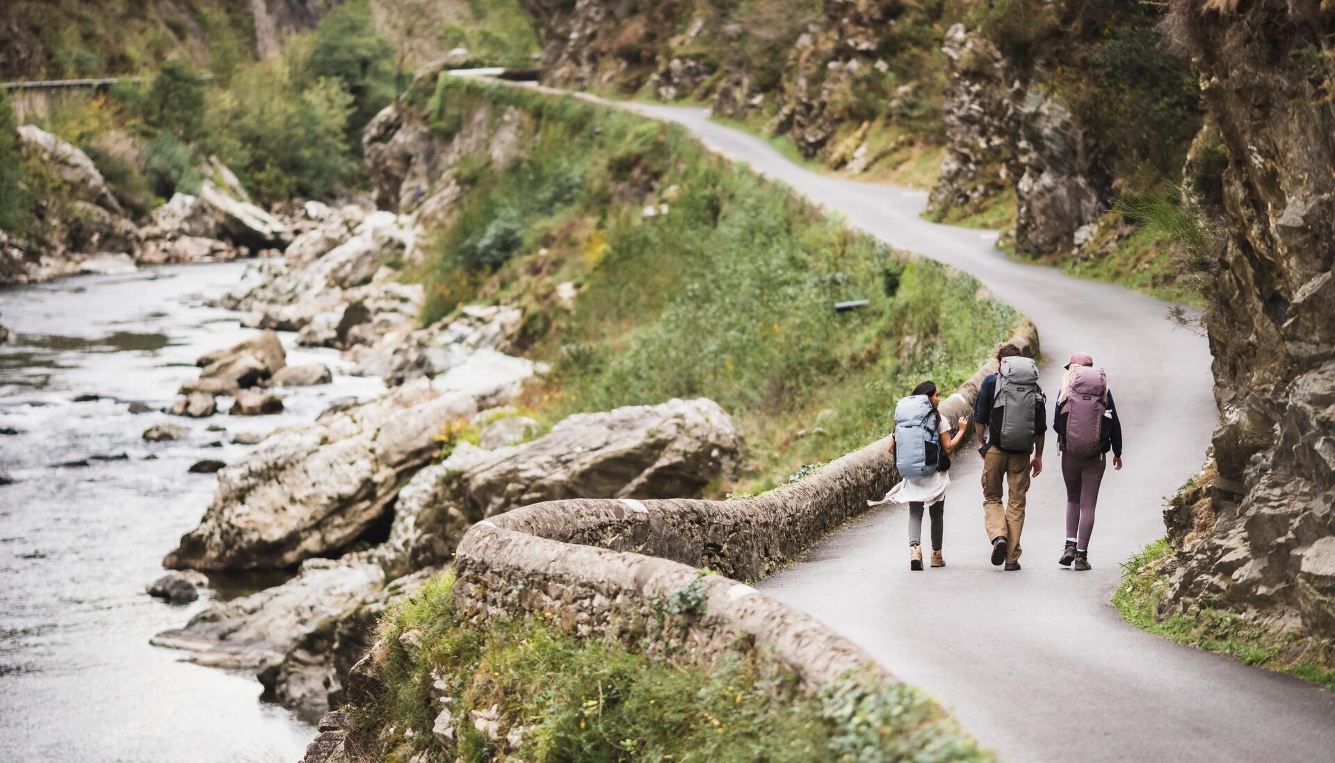 kobiety i mężczyzna idący drogą przy strumyku w odzieży outdoorowej z plecakami na plecach