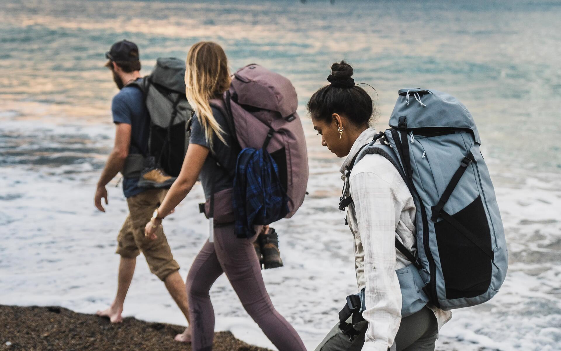 kobiety i mężczyzna idący po plaży z plecakami turystycznymi na plecach