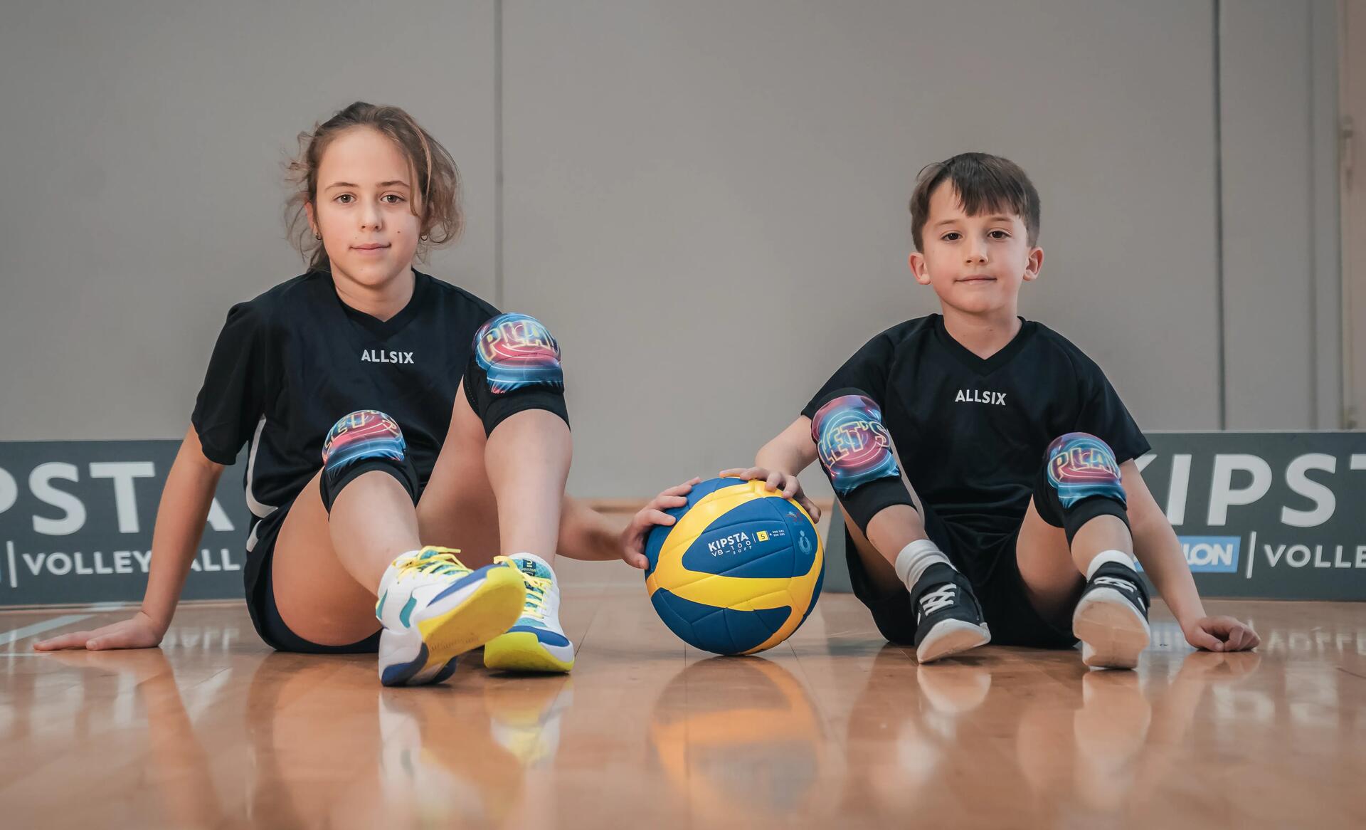 Dziewczynka i chłopiec w odzieży sportowej siedzący na podłodze hali do siatkówki przed uprawianiem aktywności fizycznej