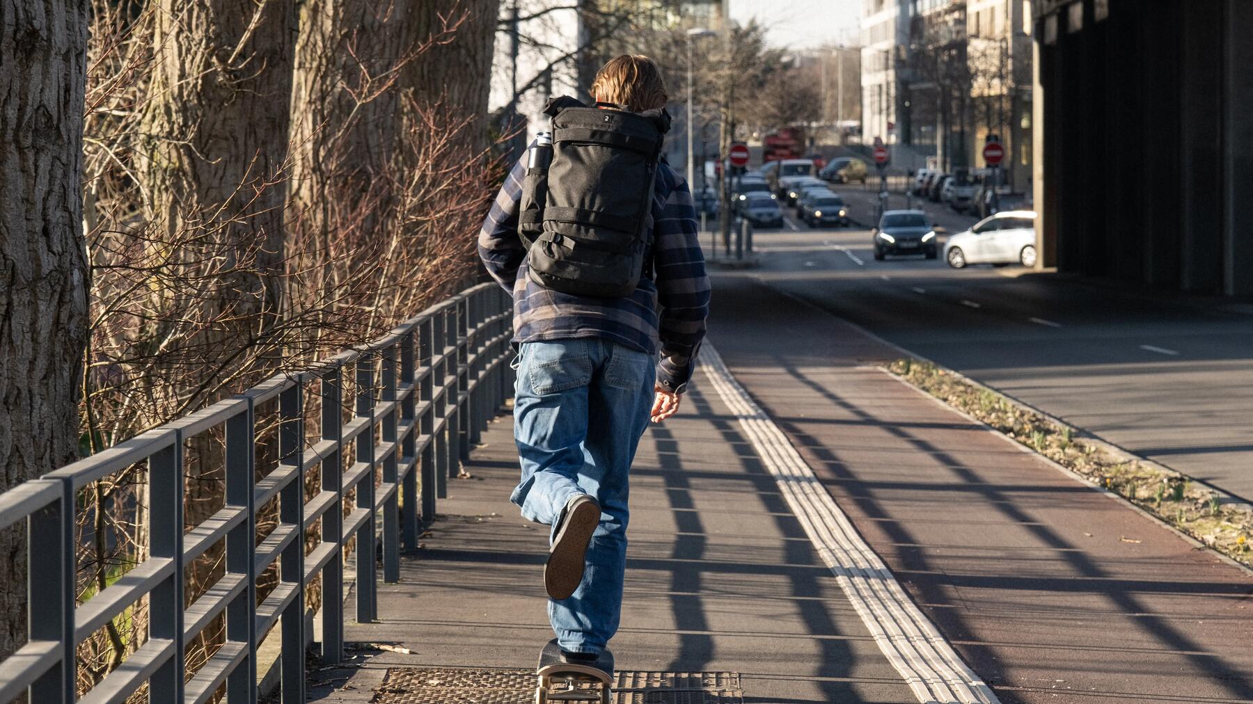 Licealista jadący na deskorolce z plecakiem do szkoły średniej na plecach