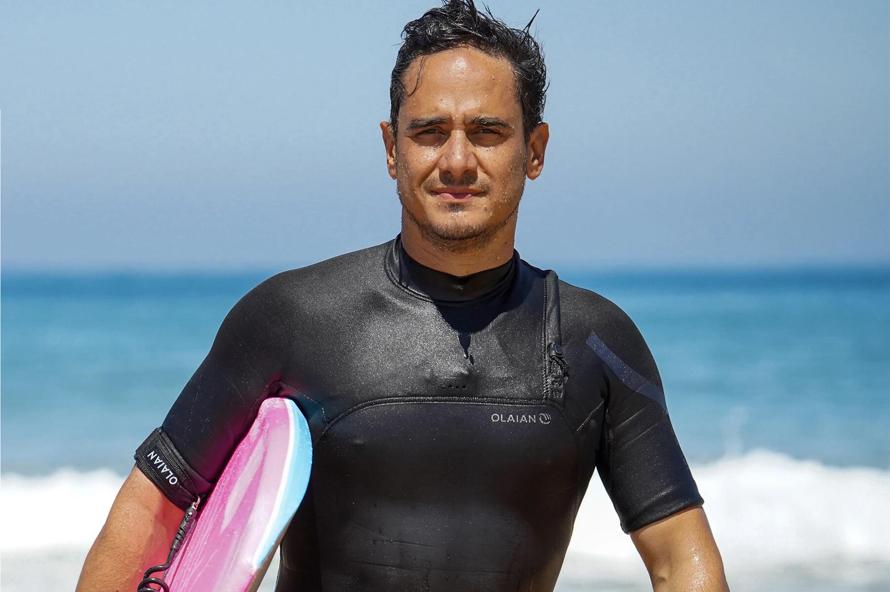 Mężczyzna w piance neoprenowej z deską bodyboardingową pod pachą wychodzący z wody po skończonym bodyboardingu