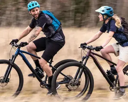 Para w kaskach jadąca rowerami po polach