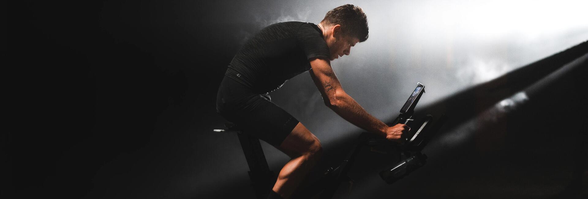 Sportowiec jadący na rowerku stacjonarnym, ma na sobie profesjonalną odzież sportową