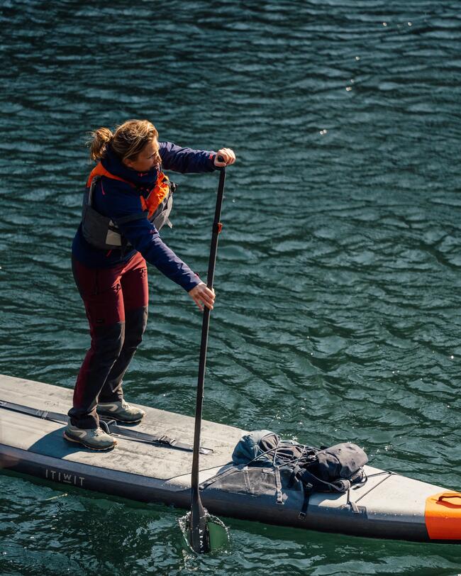 Person paddelt auf dunkelgrünem Wasser, stabile Haltung, rot-blaues Outfit, sonniger Tag, glattes, reflektierendes Wasser.
