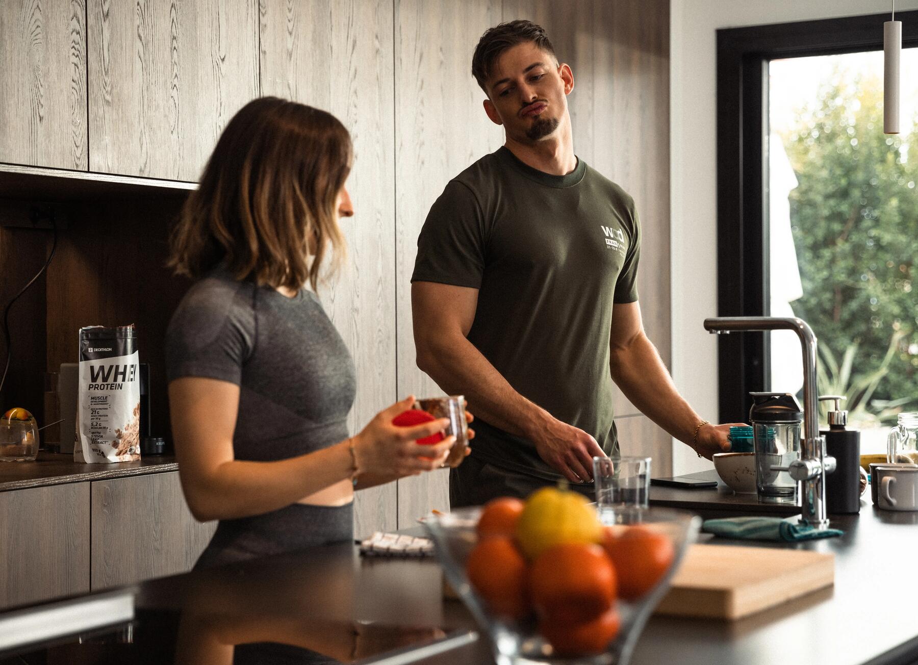Kobieta i mężczyzna w odzieży sportowej stojący w kuchni przy blacie z miską wypełnioną cytrusami