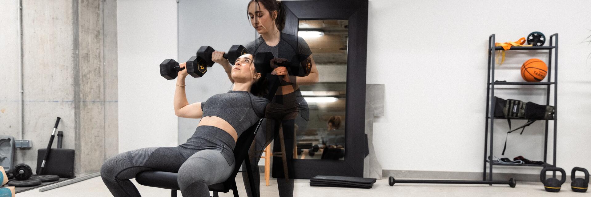 Kobieta w odzieży fitness trenująca z hantlami na ławce skośnej do ćwiczeń pod nadzorem trenerki personalnej