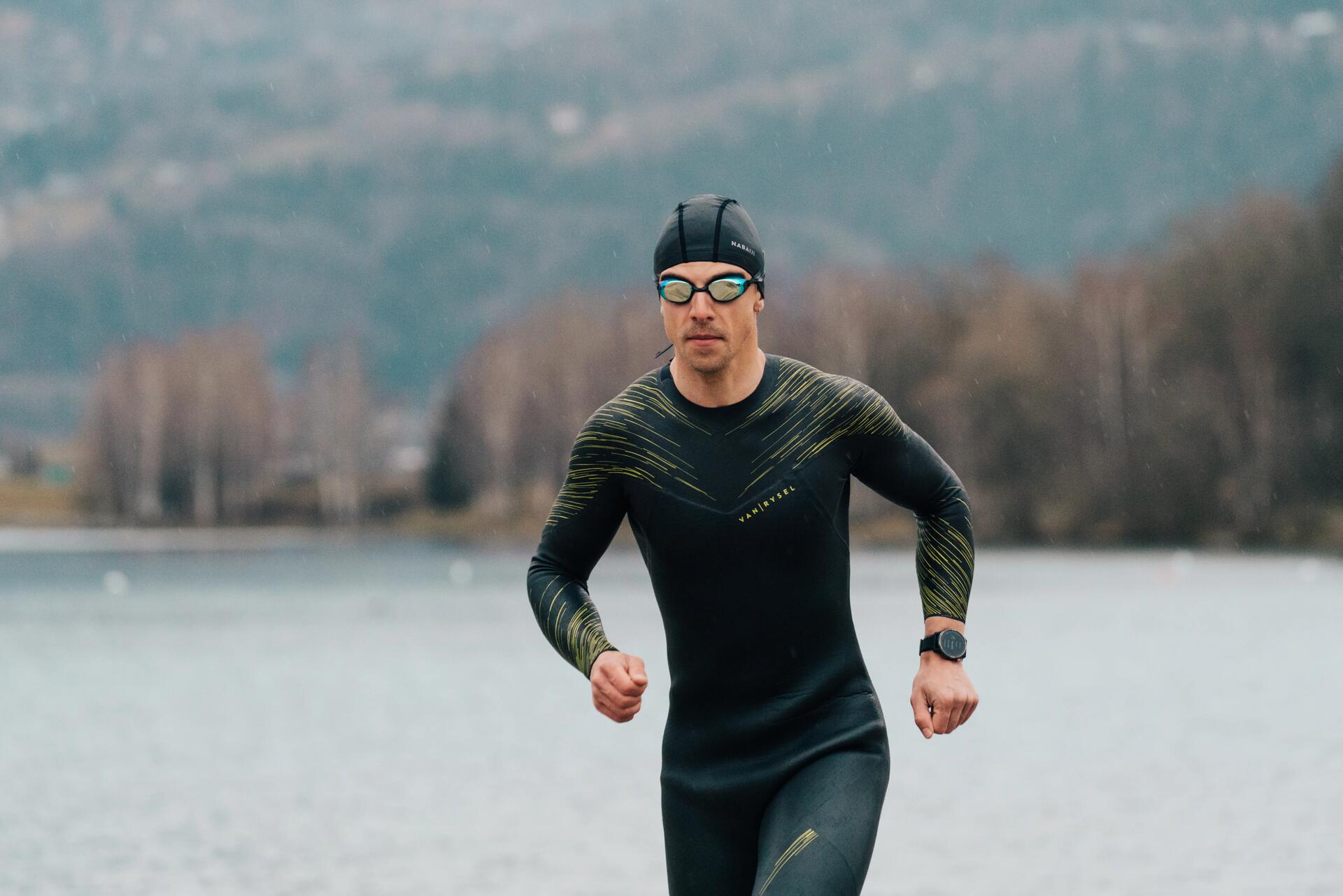 Mężczyzna w okularkach i piance pływackiej wybiegający z wody podczas treningu triathlonowego