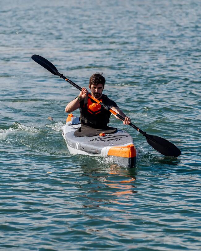 Mann im schwarz-orangenen Kajak paddelt auf blauem Wasser.