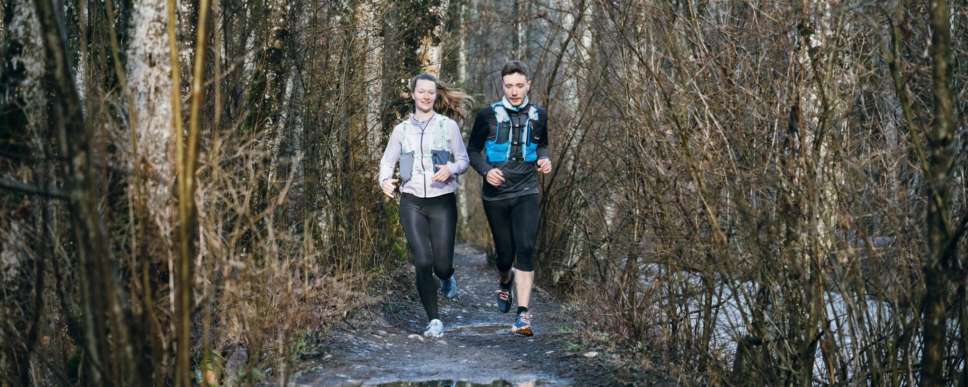 Mężczyzna i kobieta biegną w lesie w butach do biegania i z pasem do biegania