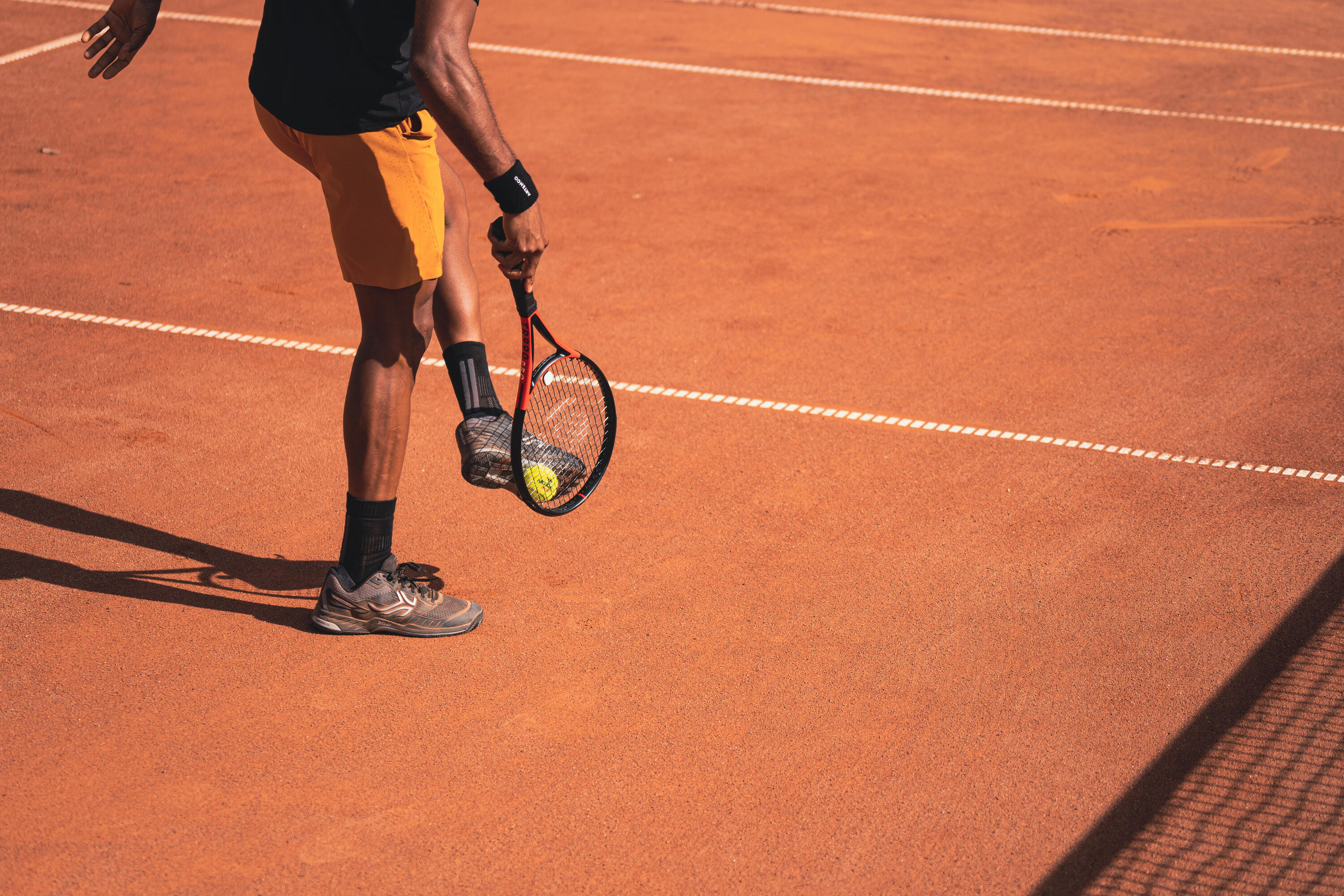 Ein Mann hebt mit seinem Schläger und seinem Schuh einen Tennisball von einem Sandplatz auf.