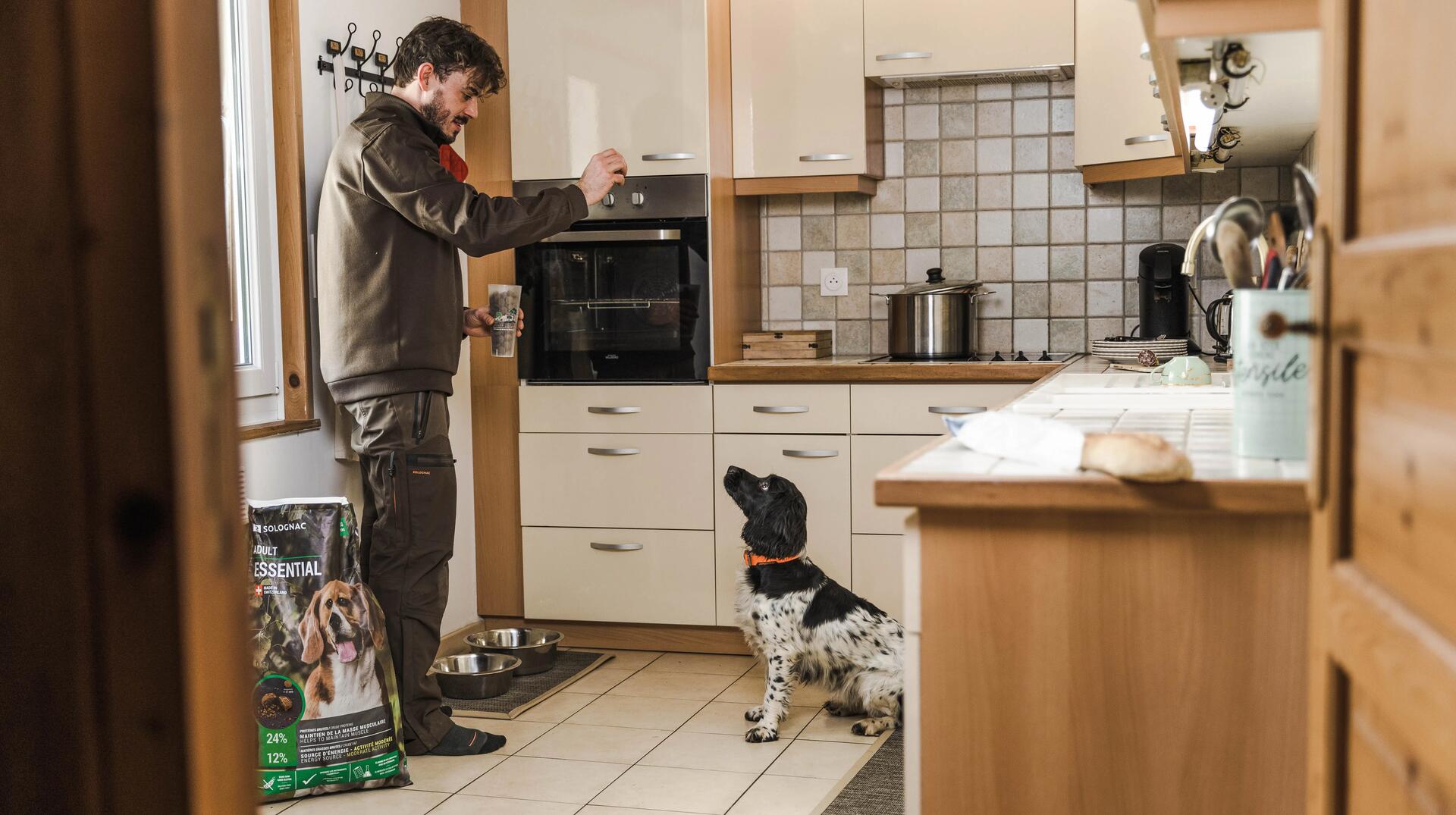 Un chasseur donne des croquettes à son chien dans la cuisine
