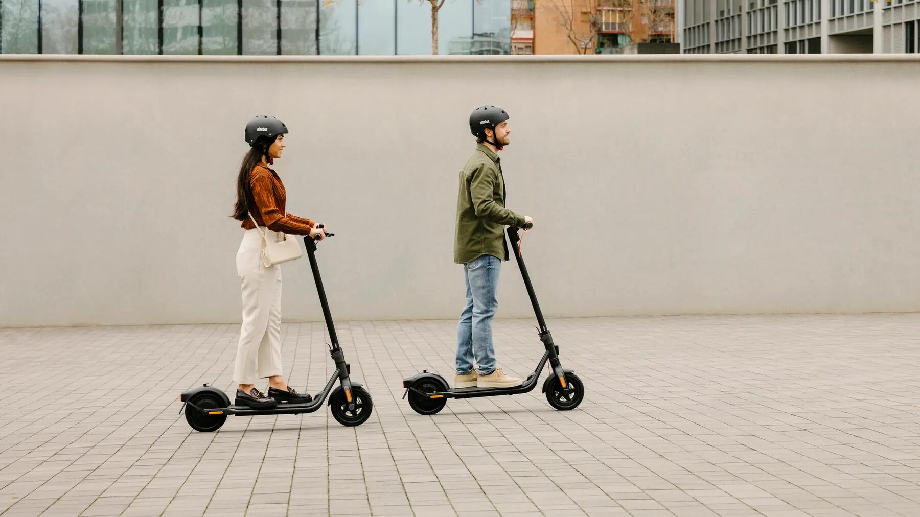 Mann und Frau gemeinsam auf zwei E-Scootern in der Stadt auf dem Asphalt unterwergs.