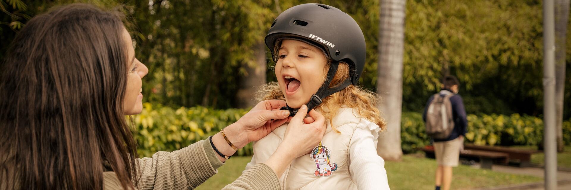 Kobieta zapinająca córce kask rowerowy dla dziecka