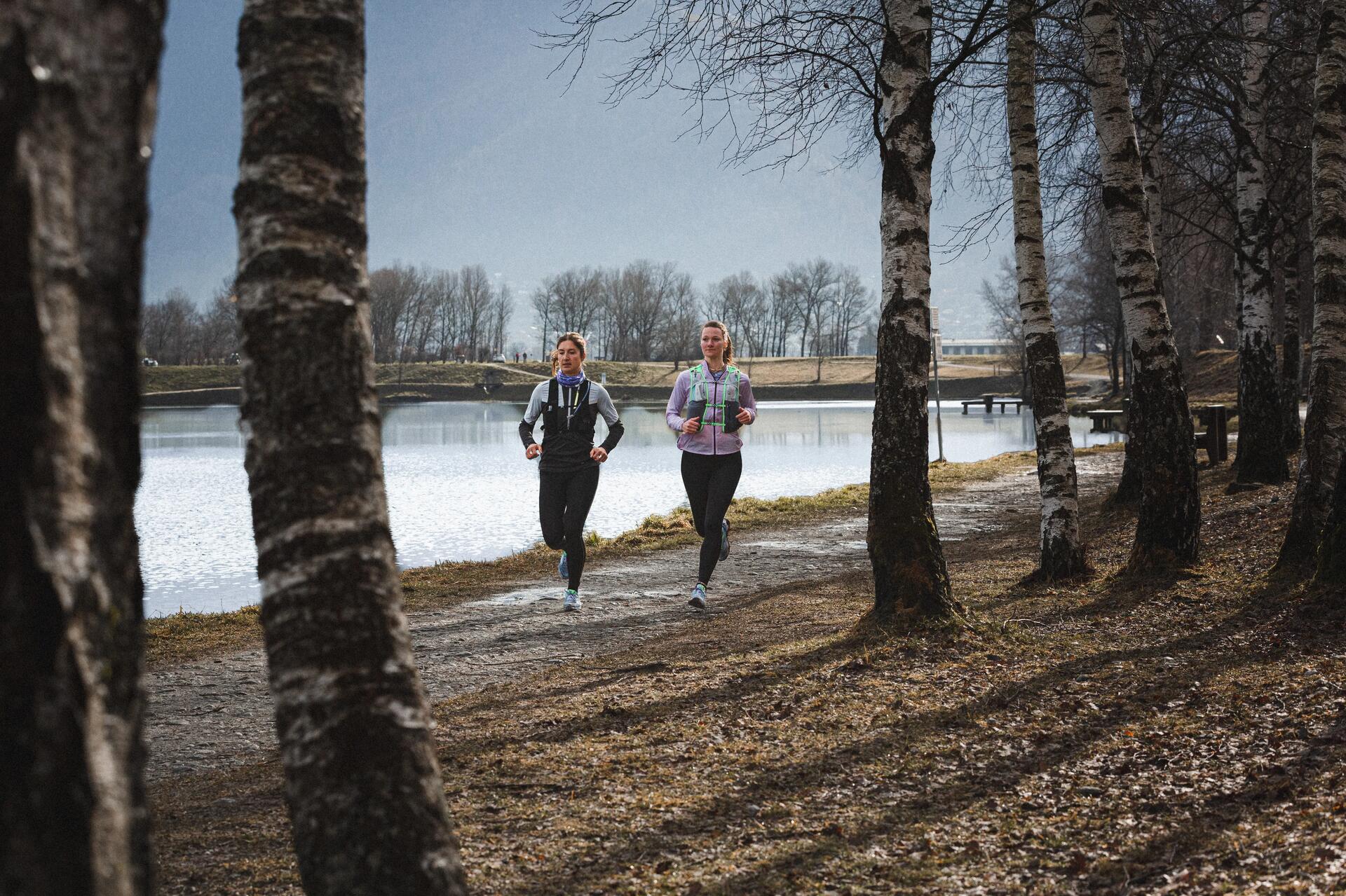 Dwie kobiety w odzieży sportowej biegające wkoło jeziora po parku