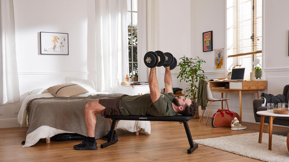 Moški v spalnici dviguje uteži na črni vadbeni klopi Corength Banc 100.