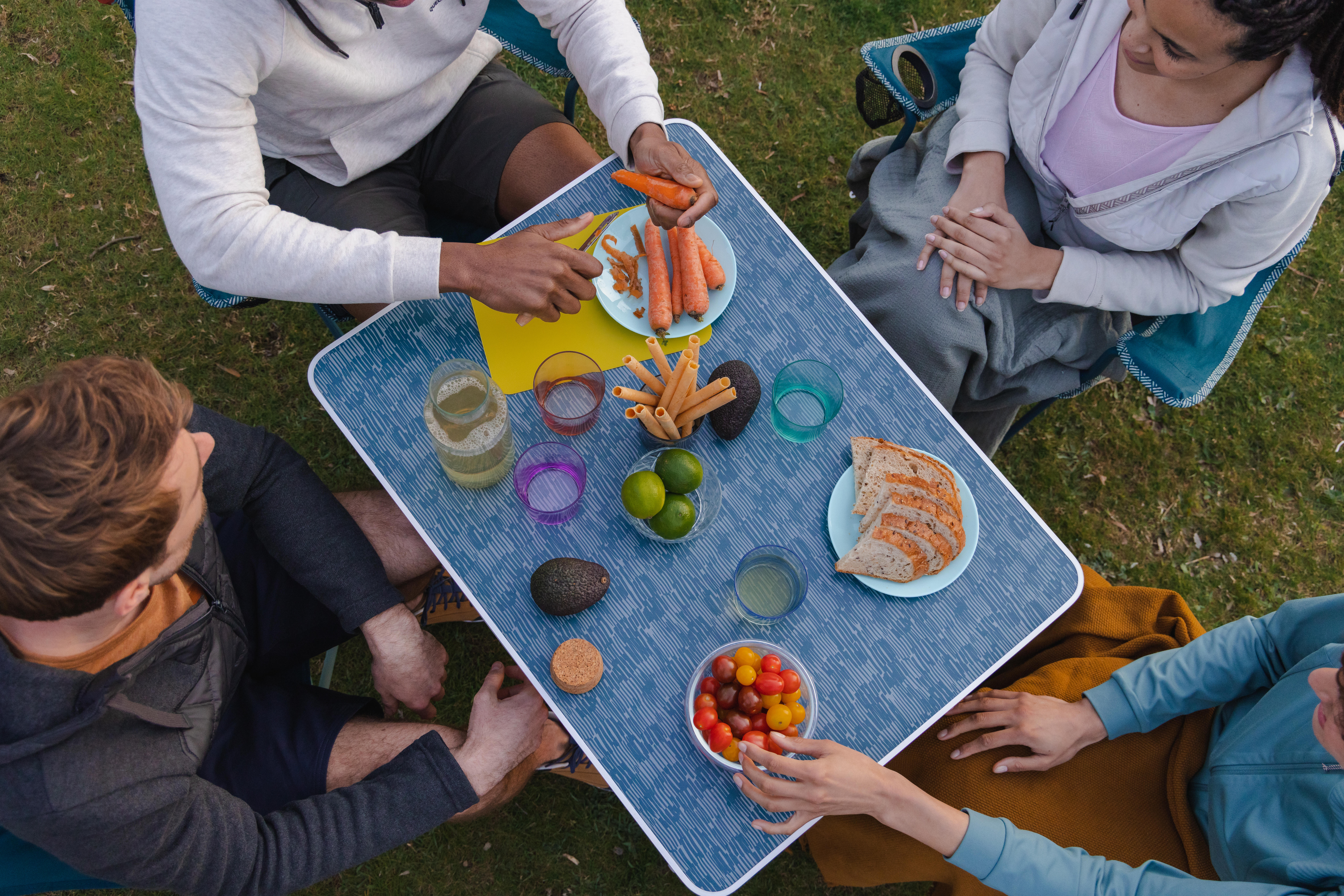Friends sharing food around a portable picnic table at a campsite