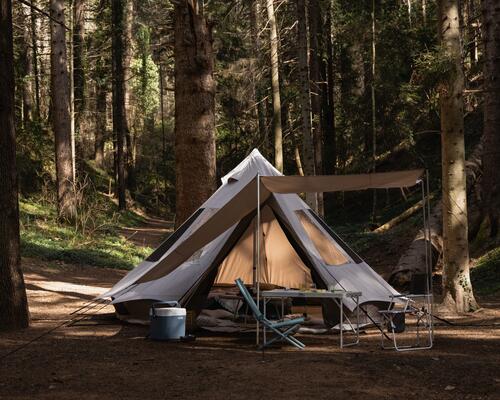 namiot i meble turystyczne rozłożone w lesie 